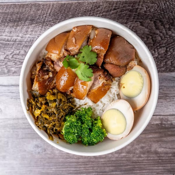 Braised pork belly, rice, broccoli, pickled mustard greens, and hard-boiled eggs in a white bowl.