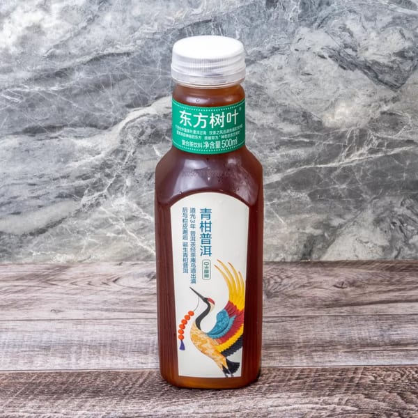 A bottle of Oriental Leaf Pu-erh tea with a colorful crane label on a marble and wood background.