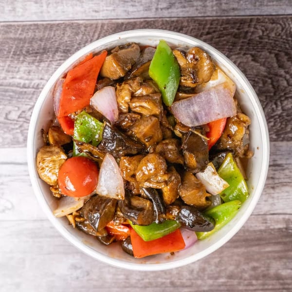 Top-down view of a white bowl filled with stir-fried chicken, peppers, onions, and mushrooms.