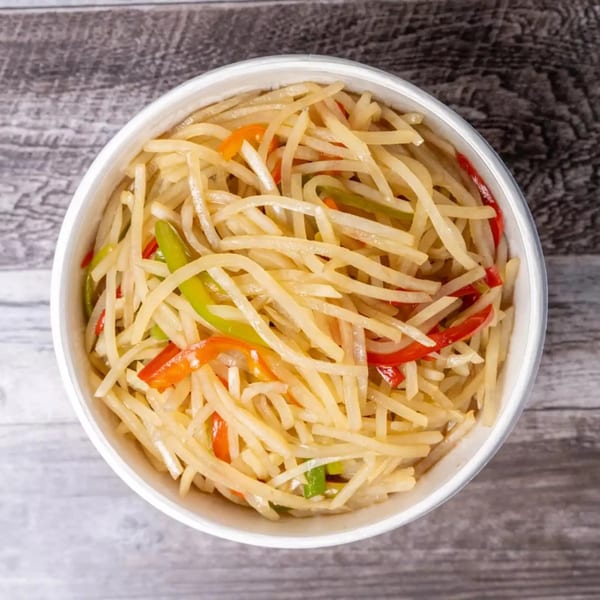 Overhead view of a white bowl filled with stir-fried julienned potatoes, red and green peppers.