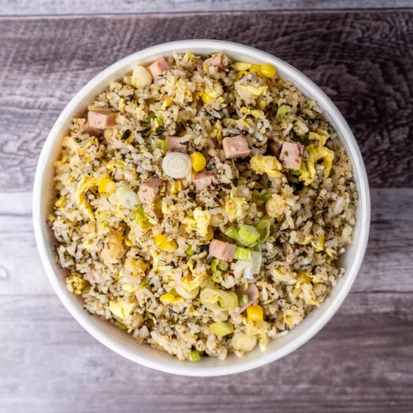 A white bowl filled with fried rice, ham, corn, egg, and green onions on a wooden table.