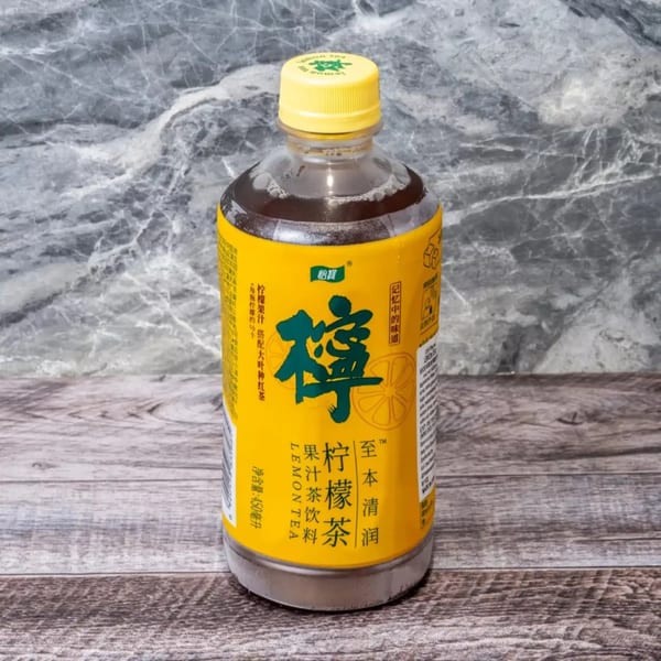 A bottle of brown lemon tea with a yellow label and cap sits on a wooden surface.