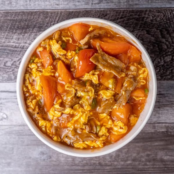 Overhead view of a white bowl filled with a savory dish of tomatoes, scrambled eggs, and meat.