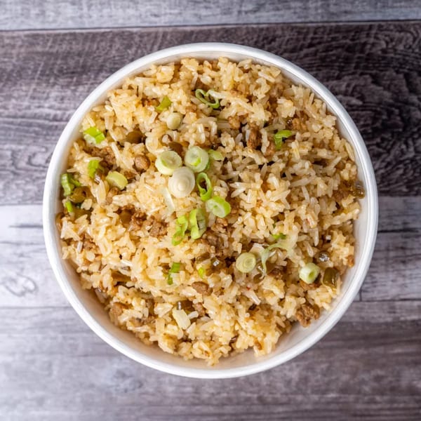 Overhead view of a white bowl filled with fried rice, garnished with chopped green onions.