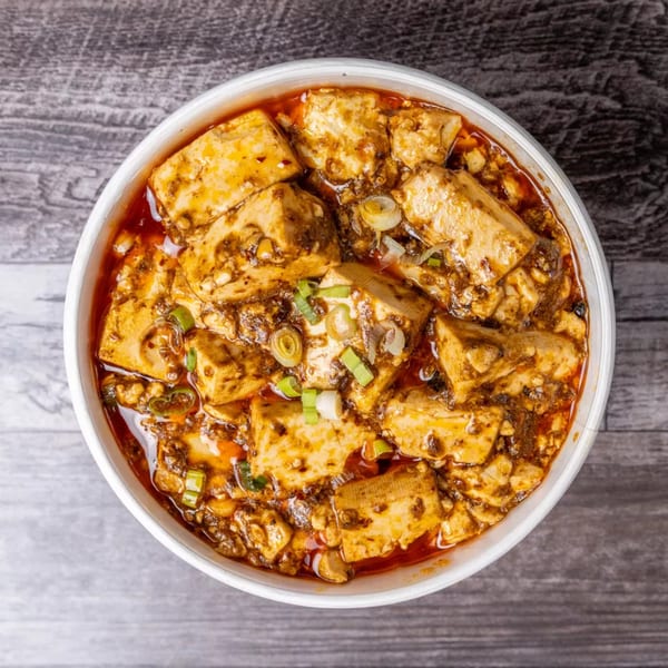 Overhead view of a white bowl filled with spicy Mapo Tofu, garnished with green onions.