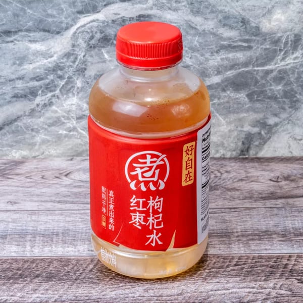 A clear plastic bottle with a red cap and red label, containing a light brown beverage.