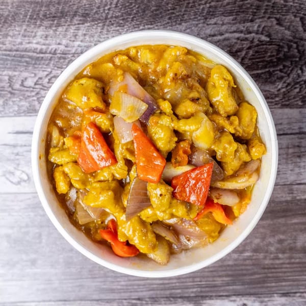 Top-down view of a white bowl filled with yellow curry, chicken, red bell peppers, and onions.
